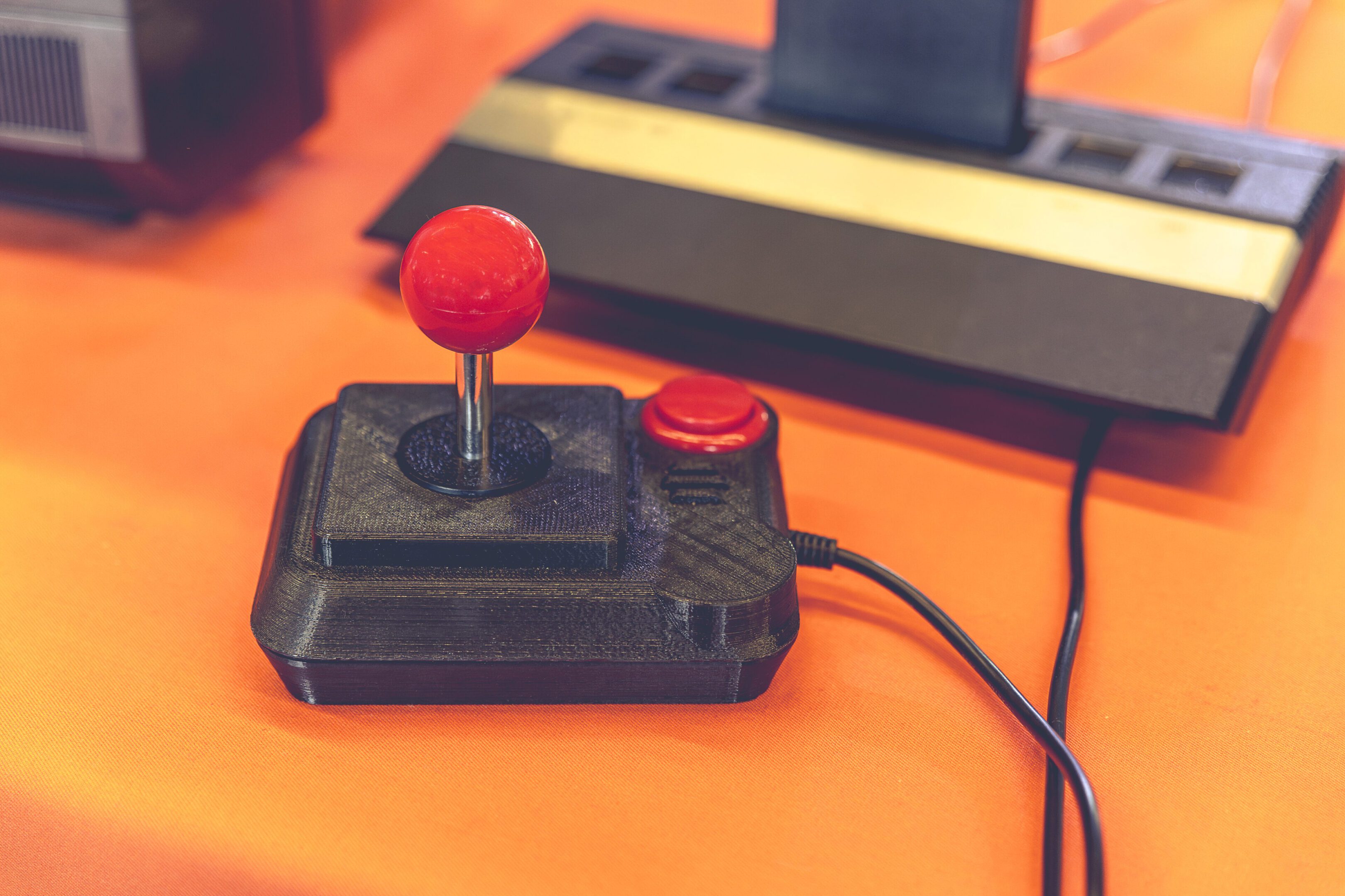 Retro Gaming Joystick and Classic 80s Console Close-Up Retro joystick and console on orange table.